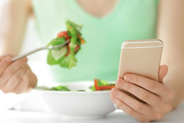 Mulher comendo salada e usando o celular