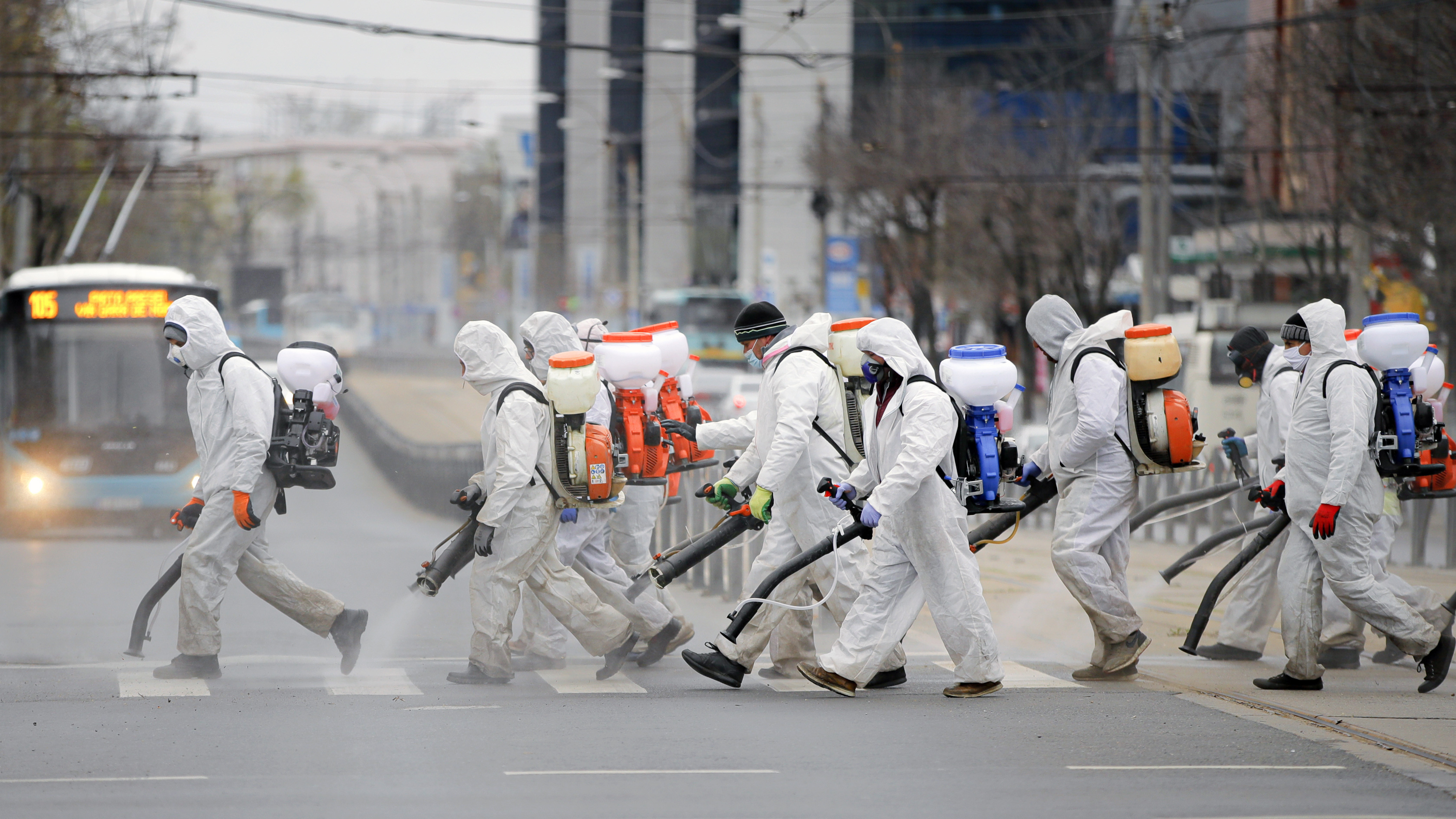 Trabalhadores municipais vestindo   roupas de proteção pulverizam produtos   químicos e desinfetam ruas em área da   capital Bucareste, na Romênia.  - Foto: VADIM GHIRDA/ASSOCIATED PRESS/ESTADÃO CONTEÚDO