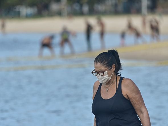 Mulher, na praia da Guarderia,  fazendo caminhada usando máscara por Vitor Jubini