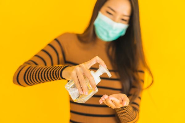 Mulher de máscara passando álcool em gel nas mãos: prevenção ao coronavírus