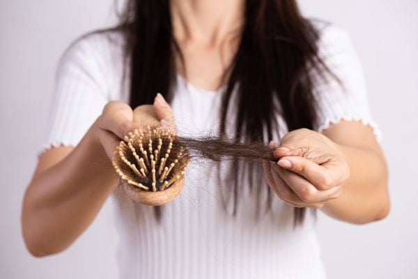 Mulher segura escova cheia de fios de cabelos; queda de cabelos tem sido comum na quarentena