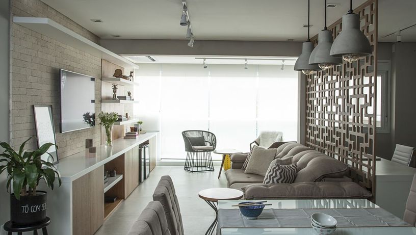Sala de jantar e sala de TV ocupam o mesmo espaço sem divisões. Atrás do sofá há uma divisória de cobogós de madeira