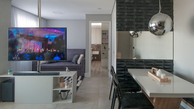 Imagem de ambiente com sala de jantar e sala de TV. A televisão está fixa em uma barra de ferro possibilitando que ela se mova entre os ambientes