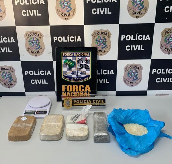 Quatro papelotes de drogas são dispostos em uma mesa, junto com a balança de precisão e um emblema da Força Nacional. 