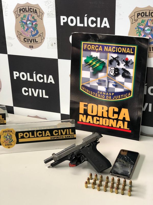 A imagem mostra uma arma com 24 munições em cima de uma mesa com os símbolos da Polícia Civil e da Força Nacional.