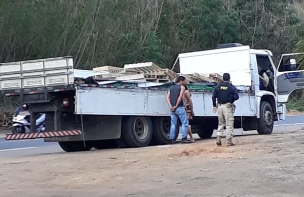 A imagem mostra o caminhão no qual as drogas estavam escondidas, com um agente da PRF e outro homem na frente do veículo.