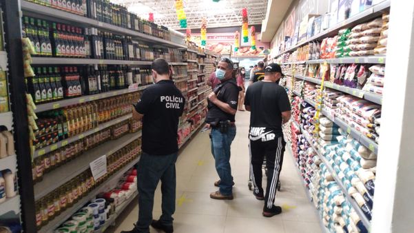 A imagem mostra fiscais do Procon analisando produtos em prateleiras de um supermercado