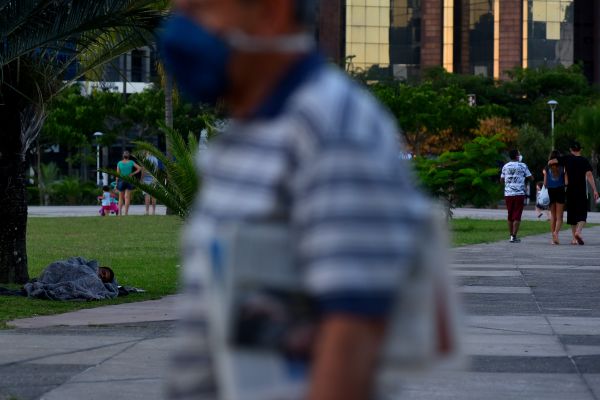 Homem dorme na grama enquanto pessoas circulam na Praça do Papa por Fernando Madeira