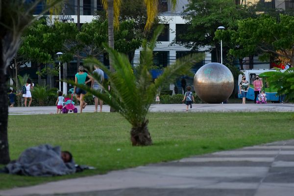 Homem dorme na grama enquanto famílias levam crianças para brincarem na Praça do Papa por Fernando Madeira