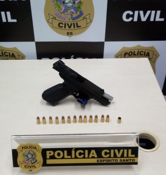 A imagem mostra uma pistola com 13 munições em cima de uma mesa, com o distintivo da Polícia Civil a frente.