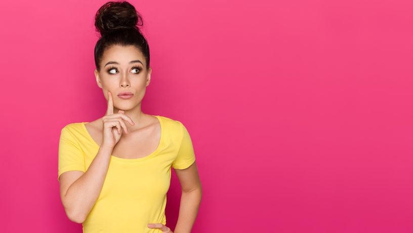 Mulher indica que está pensando; ao fundo, parede rosa