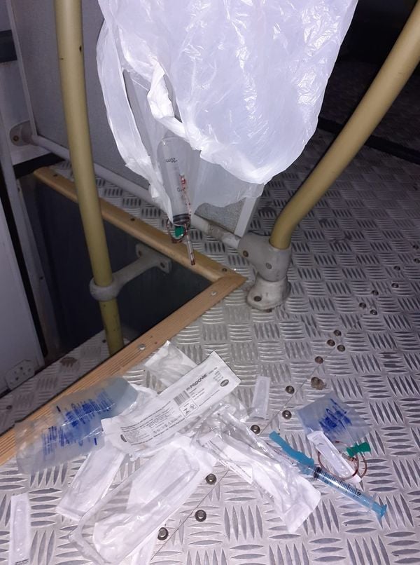 Uma sacola rasgada com seringas sujas no chão de um coletivo