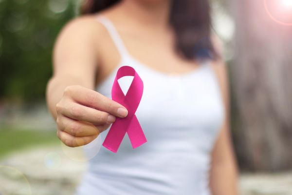 Mulher segurando laço rosa, símbolo da campanha de prevenção ao câncer de mama; outubro rosa