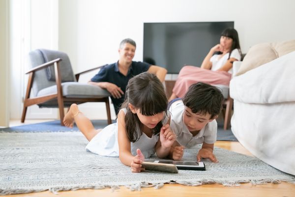 Crianças usando tablet e sendo observadas pelos pais