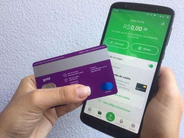 Usuário segurando um cartão de crédito e um celular com aplicativo financeiro aberto