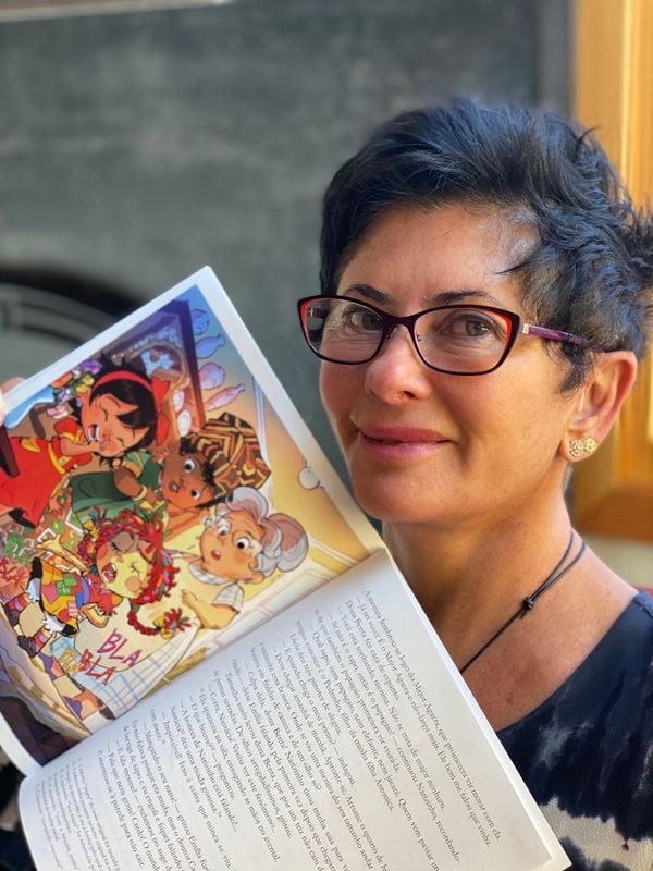 Cleo é uma mulher branca, de óculo, que segura um livro com uma ilustração dos personagens do Sítio do Picapau Amarelo.