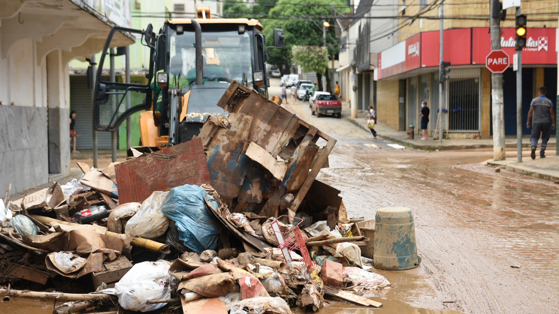 As ruas ainda estão cobertas de lama. Um trator junta  lixo, móveis e objetos que foram arrastados pela chuva. Bairro Centro