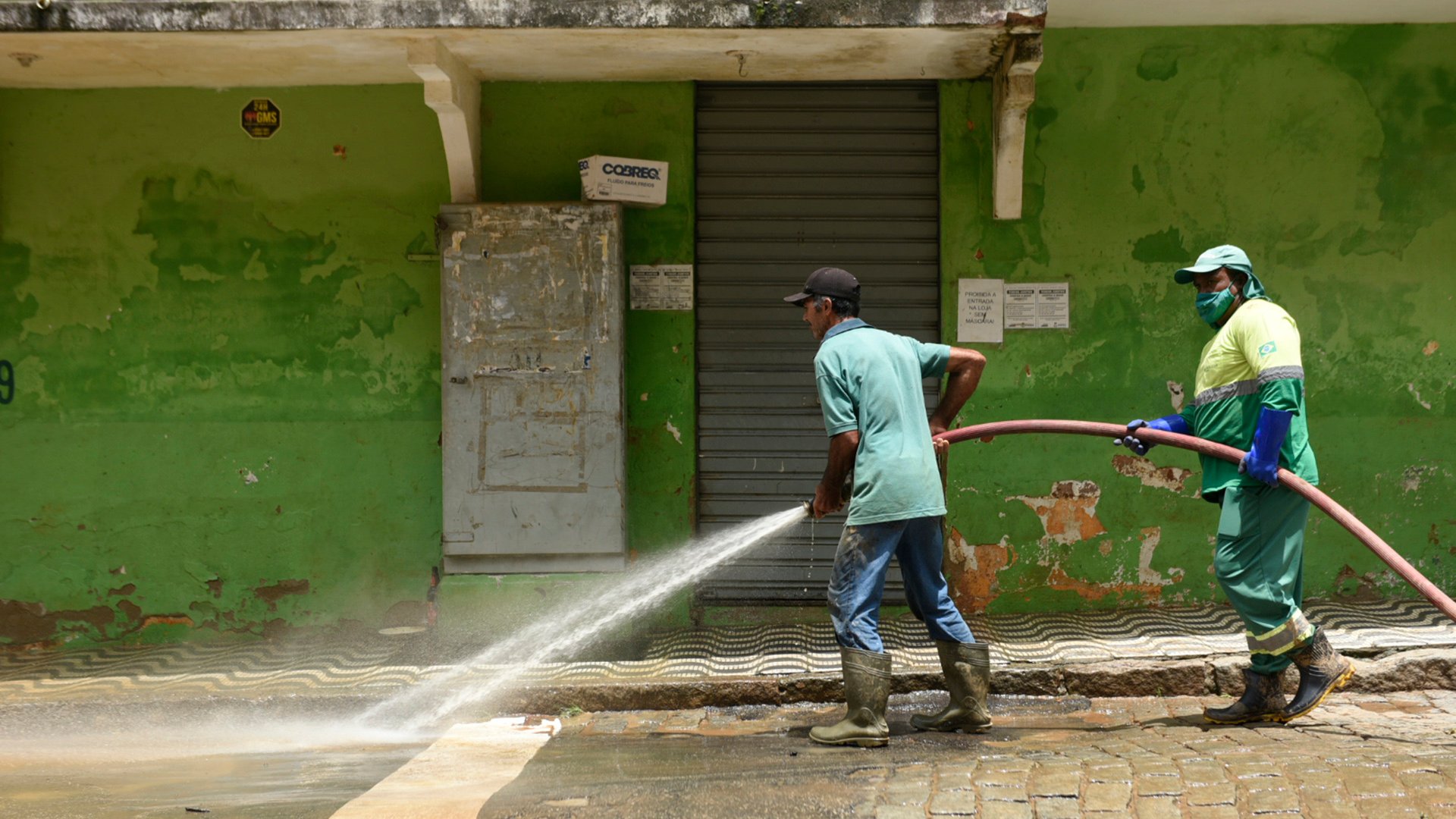Funcionários da prefeitura limpam as ruas usando uma mangueira