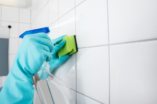 Pessoa limpando azulejos com borrifador e esonja 