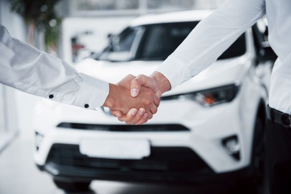 Homens dando as mãos em frente a um carro ao fechar uma venda do automóvel. 