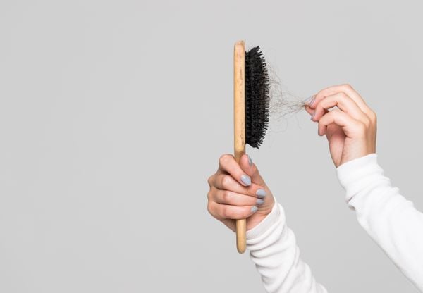 Pessoa retirando cabelos da escova / queda de cabelo