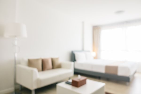 Imagem desfocada da sala de um apartamento com um sofá branco e almofada marrom.
