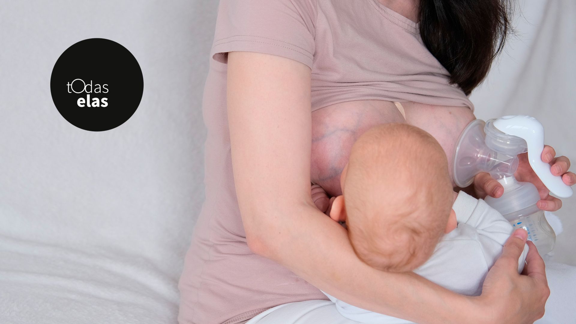 Mãe com filho recém-nascido segurando-o nos braços usando bomba tira leite