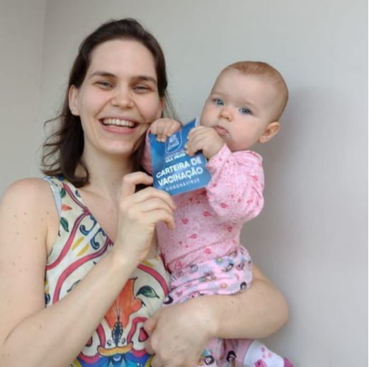 Andreia Foeger, 32 anos, e a filha Beatriz, de 10 meses, com a carteira de vacinação da mamãe em mãos. Crédito: Andreia Foeger/ Acervo pessoal
