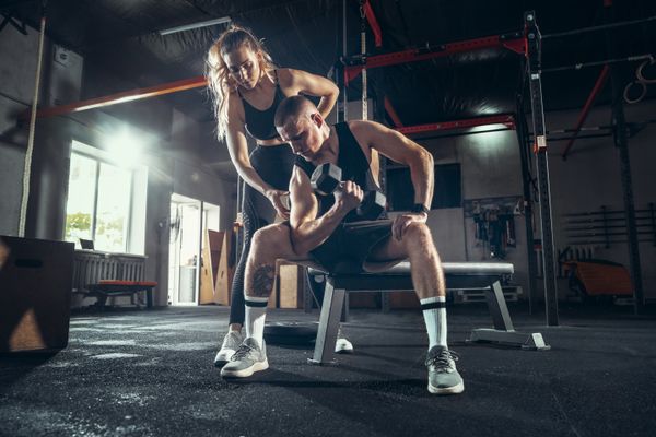 Mulher instruindo a atividade física de um homem sentado em um banco em uma academia