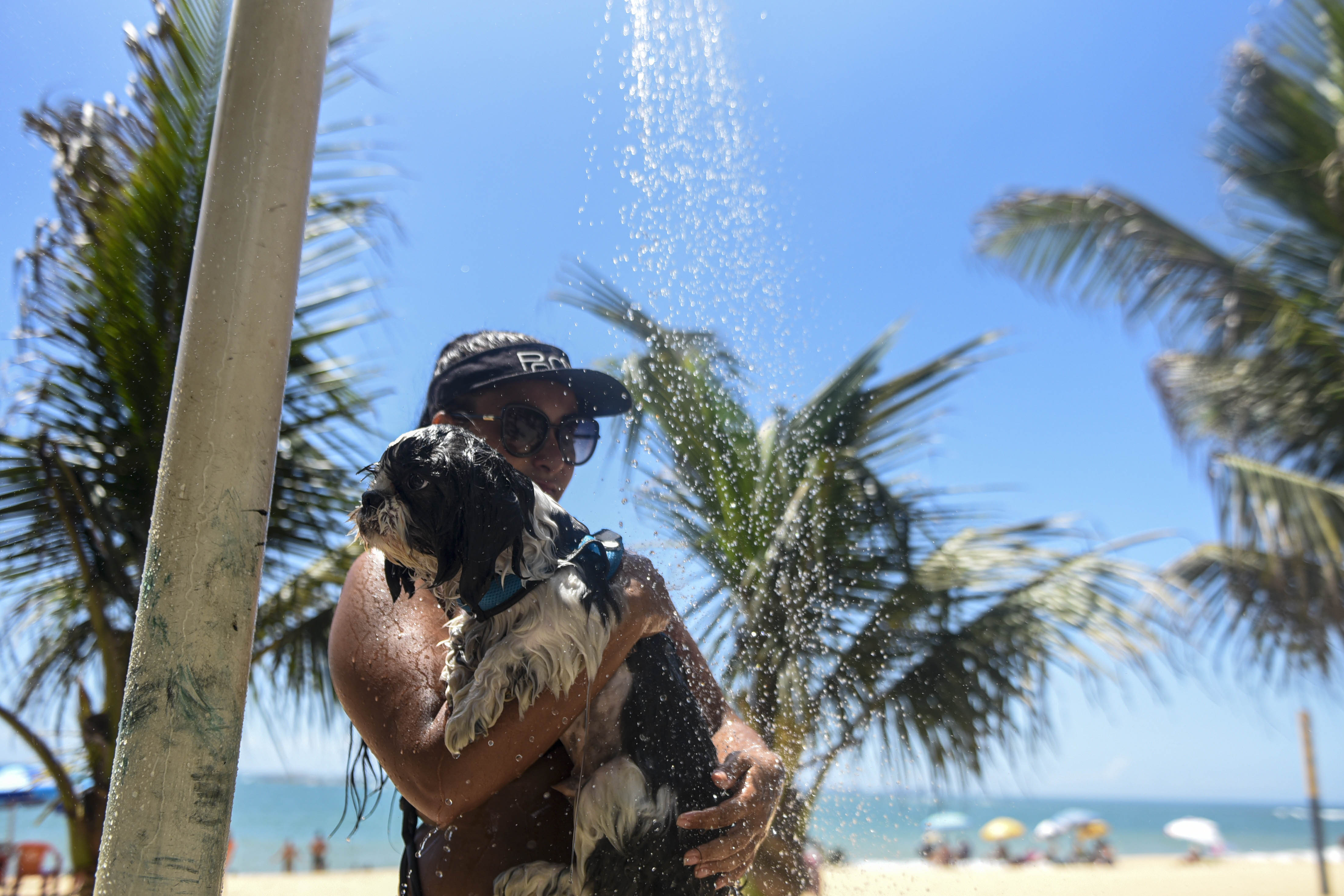 Mulher noma ducha com seu cachorro na Praia de Itapuã