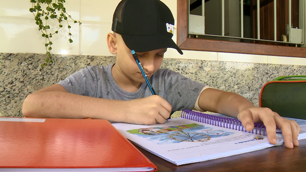 O menino recebe as atividades da escola e estuda em casa com o apoio da família