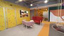 Ambiente corporativo com paredes amarelas, dois sofás assimétricos, um vermelho e outro rosa no centro. No canto direito há um balanço. (Projeto de Melissa Francani)