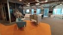 Ambiente corporativo em open space com piso laranja e dois sofás, um azul e um cinza. (Projeto de Melissa Francani)