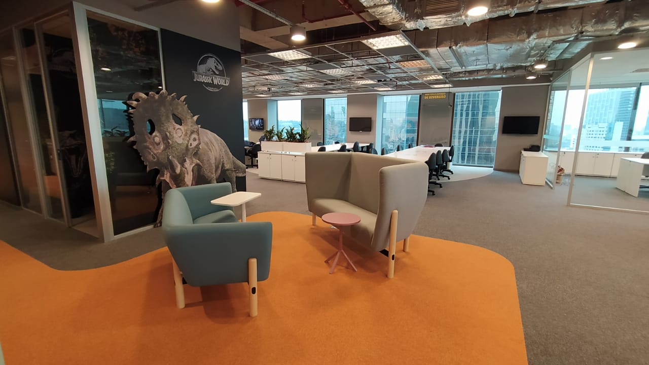 Ambiente corporativo em open space com piso laranja e dois sofás, um azul e um cinza. 