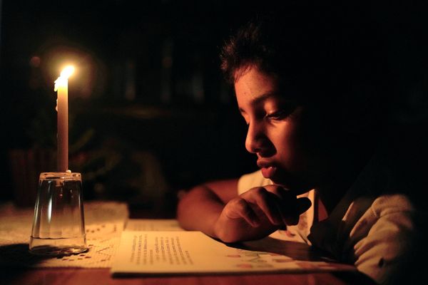 O pequeno Lorenzo, de 8 anos, aproveita a pouca luz da vela para estudar
