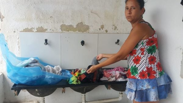 Ludmila Bispo com pilha de roupas sem lavar devido à falta de água em Guarapari