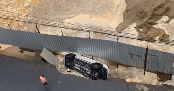 Um homem ainda aparece na imagem com uma corda amarrada na lateral da caminhonete, tentando evitar a queda. O veículo, no entanto, caiu no espaço entre o asfalto e os tapumes