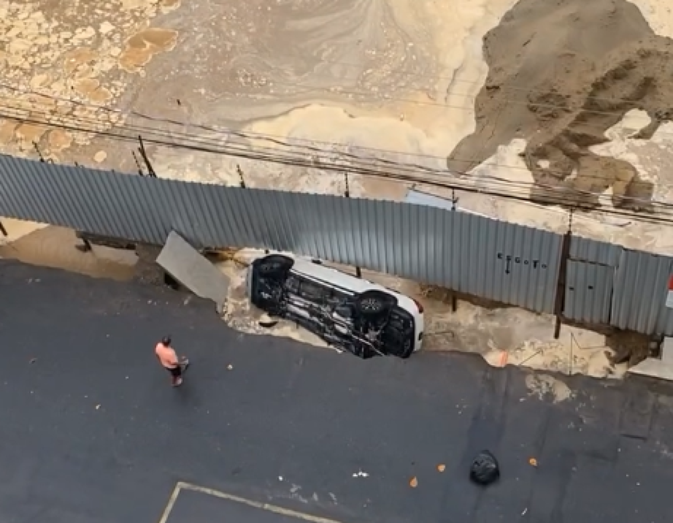 Um homem ainda aparece na imagem com uma corda amarrada na lateral da caminhonete, tentando evitar a queda. O veículo, no entanto, caiu no espaço entre o asfalto e os tapumes