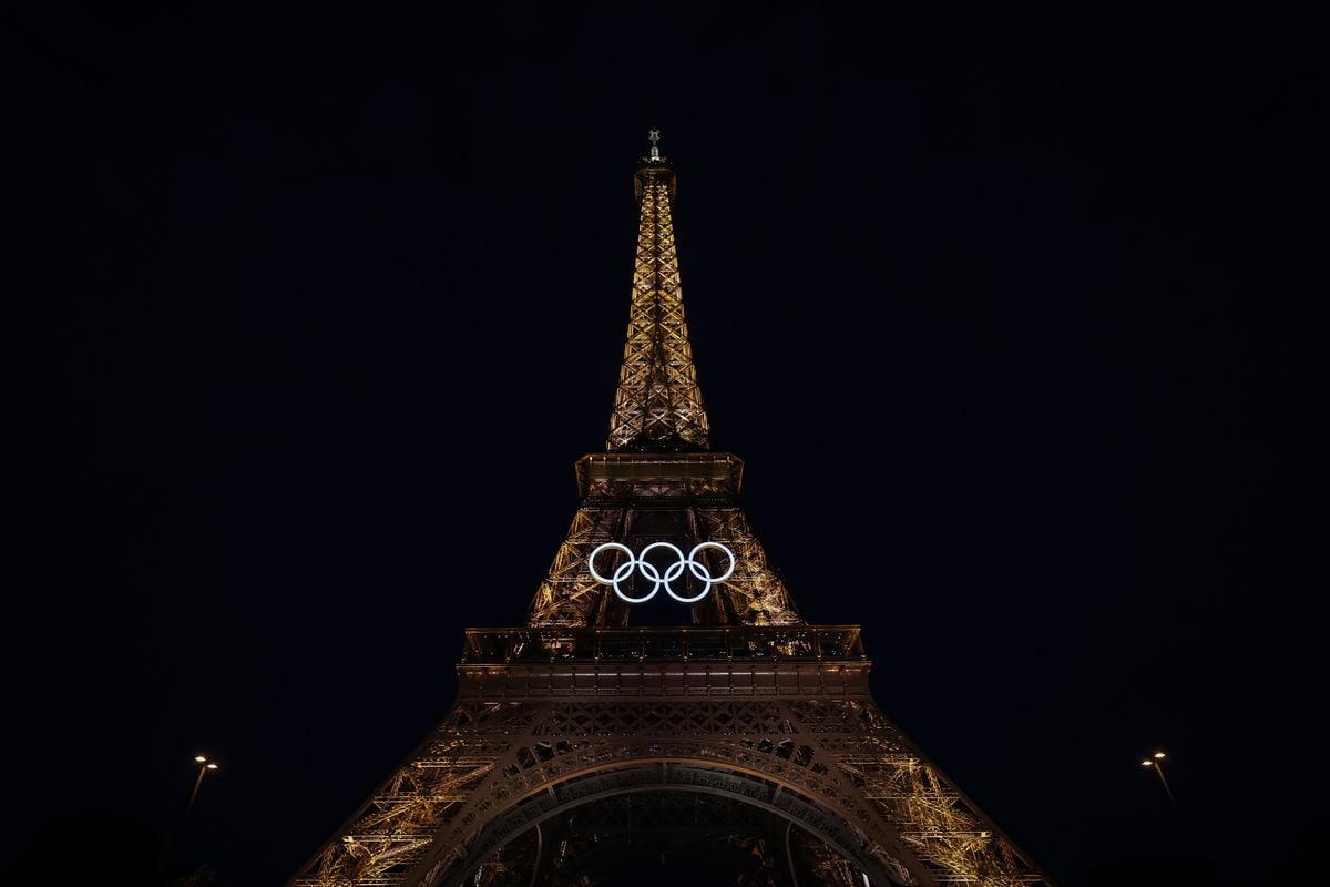 Torre Eiffel à noite iluminada com os arcos olímpicos ao centro dela
