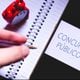 The word Civil service exam ( Concurso PÃºblico ) in Brazilian Portuguese  written on cell phone screen. A man holding a pen, a notebook and a clock in the composition.