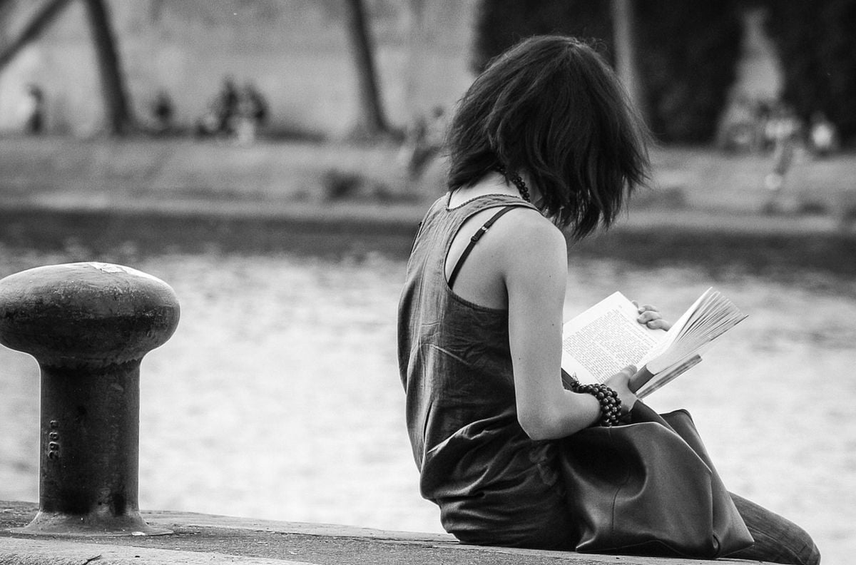 Mulher lendo um livro:  'A cobrança e a responsabilidade interna geradas pelo desejo de prosperar academicamente me levaram a uma conclusão exagerada, típica do meu hiperfoco inseguro: ler ficção era um desvio de percurso desnecessário, prejudicial ao processo de criação formal e mecânico da pesquisa'