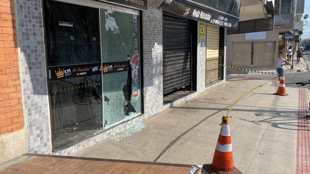 A vítima estava em frente à barbearia, cuja porta preta aparece fechada na imagem. Os tiros atingiram a vidraça da loja ao lado