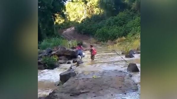 Chuvas dos últimos dias fez o nível subir, o que obrigou a mulher a entrar na água com a criança para chegar ao outro lado da estrada