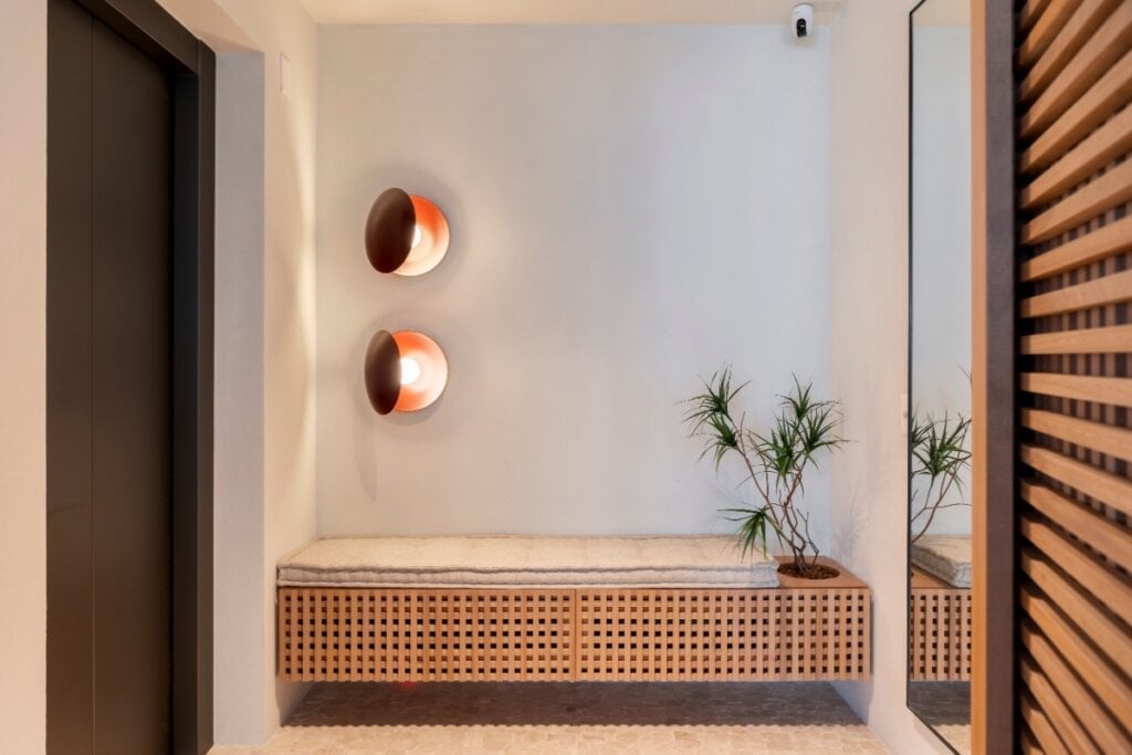 O banco suspenso com portas em muxarabi une estética, funcionalidade e ventilação no hall (Projeto: Rawi Arquitetura + Design | Imagem: Rafael Renzo)