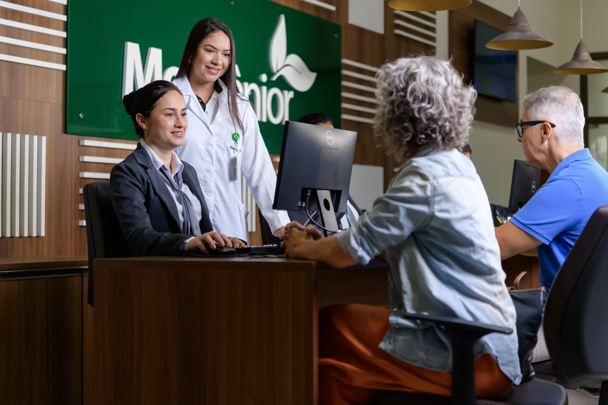 Casal de idosos sendo atendido com logo da MedSênior ao fundo