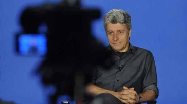 Jornalista Caco Barcellos posicinado frente a uma câmera de gravaçlão 