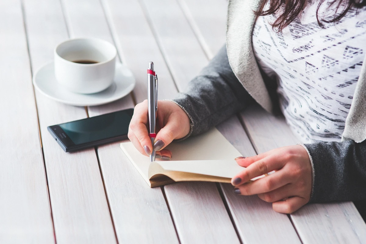Jovem escreve em caderno, educação financeira, café