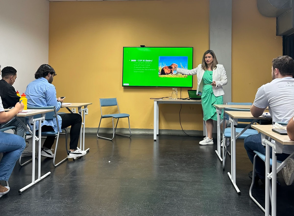 Dani Klein mostra imagem numa tela a estudantes sentados nas carteiras em uma sala de aula.