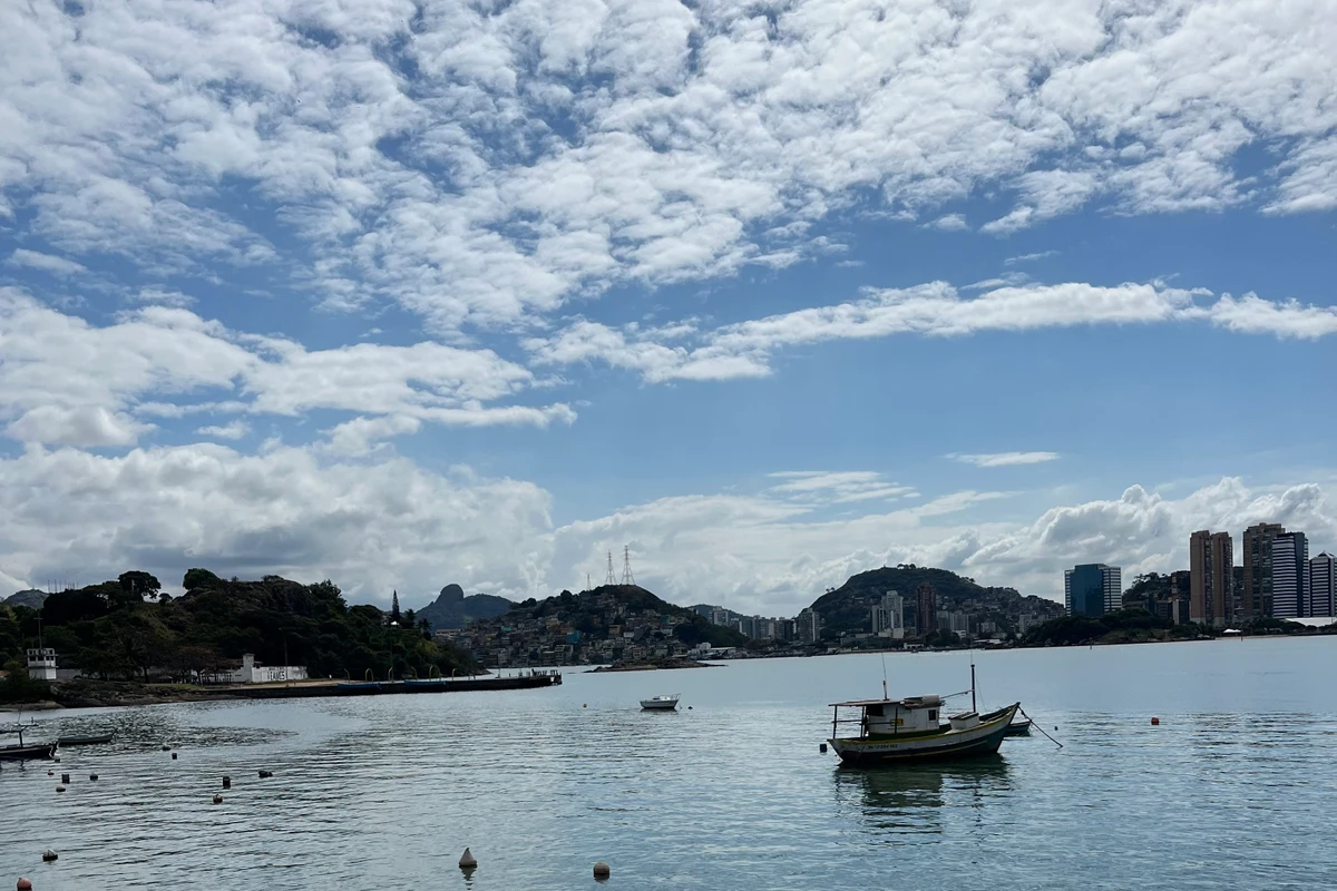 Imagem da baía de Vitória com um barco em evidência e a cidade ao fundo.