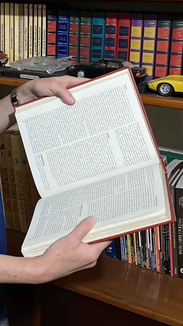 Volume da enciclopédia aberto na mão de uma pessoa.